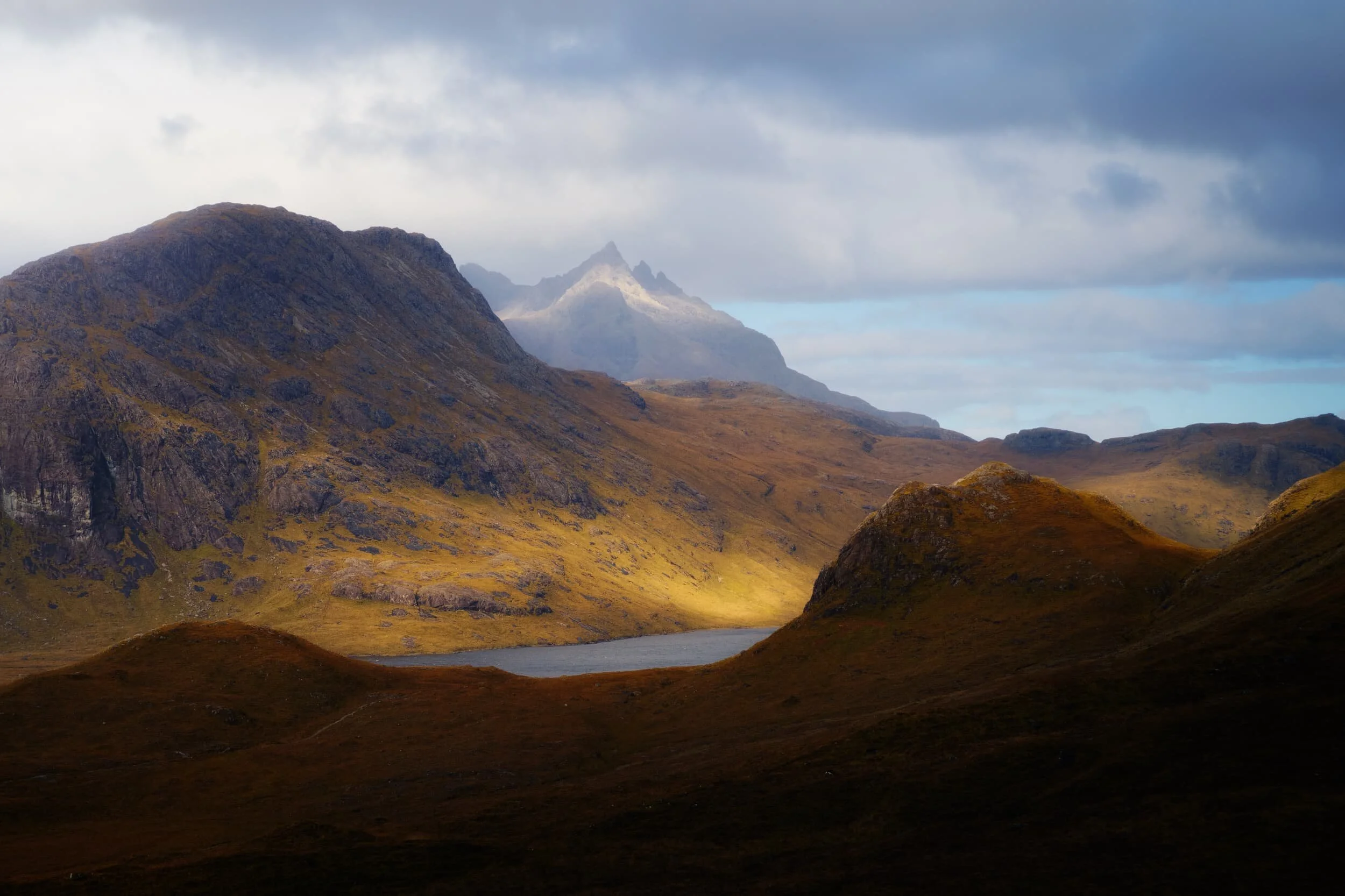 A particularly strong burst of light breaks through the low clouds as I shot this view across Loch na Creìtheach . The hill on the left is Sgùrr Hain (420 m/1,377 ft) and the crown-like summit in the distance is Sgùrr nan Gillean (966 m/3,170 ft), one of Skye’s most famous peaks. Its name translates from Scottish Gaelic as “peak of the young men”.