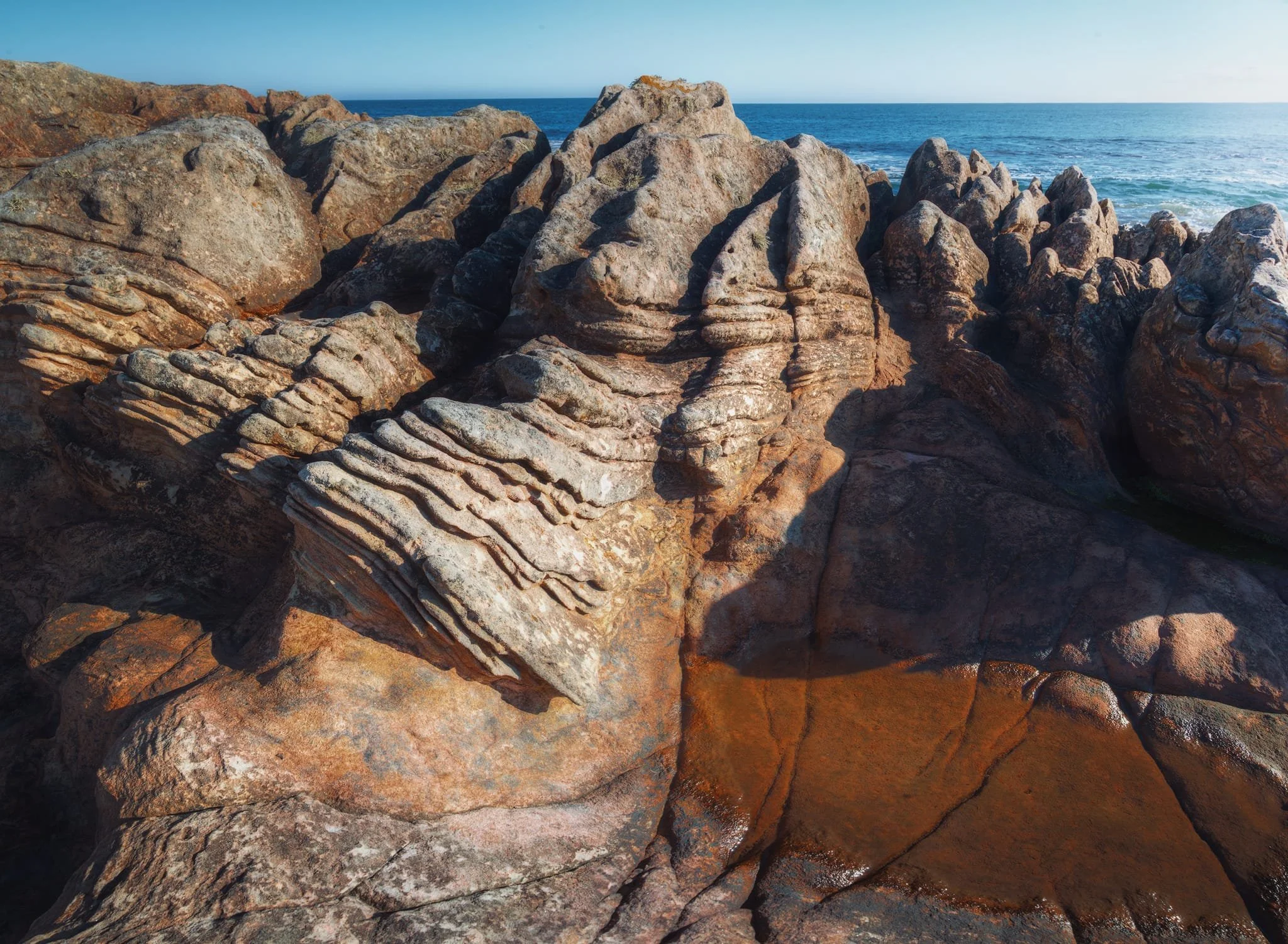 A panorama of five vertical shots, stacked left to right, shows the impressive layers of sedimentary rock made of pinkish-brown sandstone. The layers form ridges that tell the story of how this rock was formed. Some of the rock is tilted as well, having been affected by movements in the Earth’s crust. You can also see different patterns of cracks in the rock, creating angular pieces that have weathered over time into various colors. Nature is an artist.