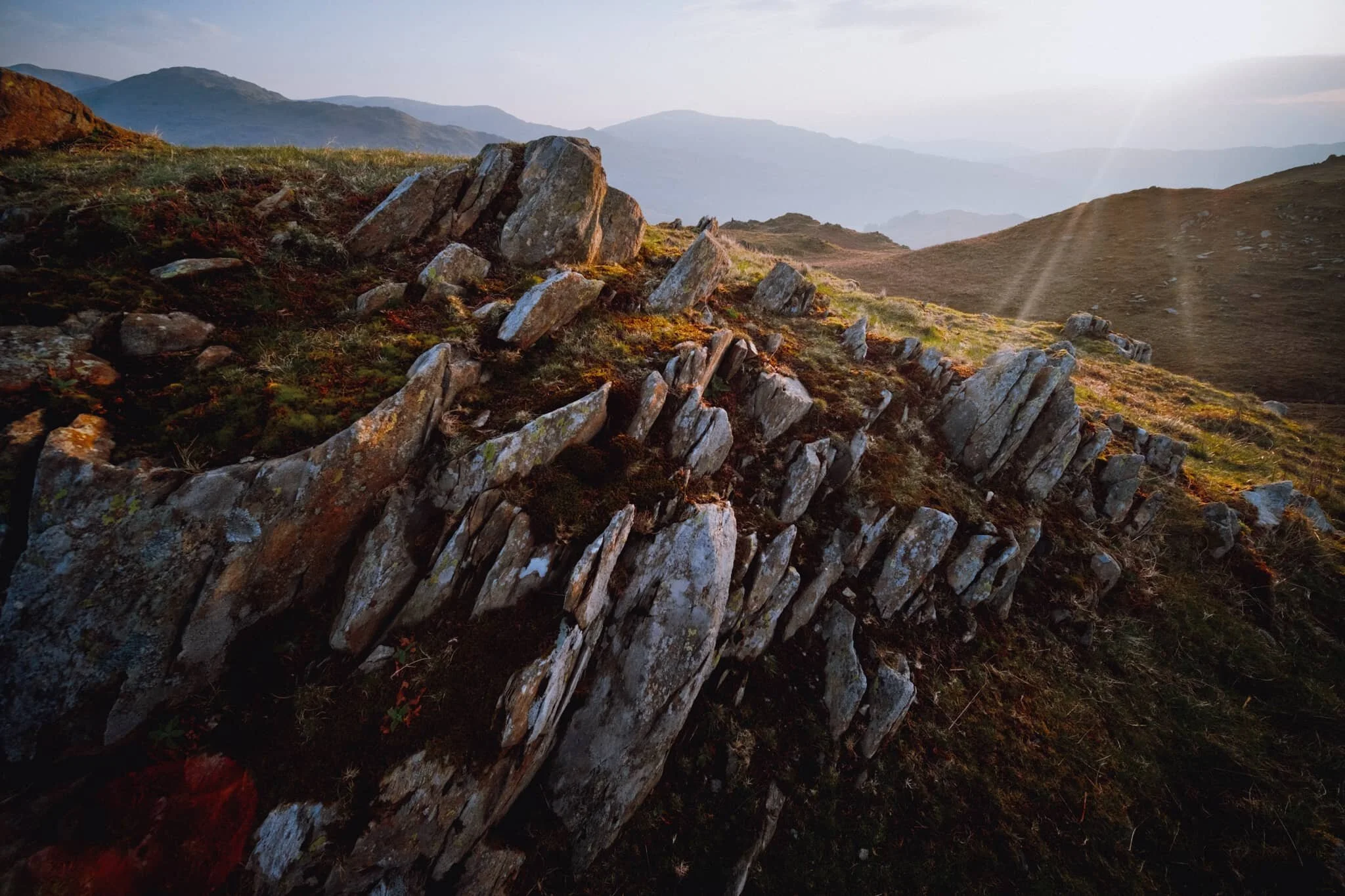 The summit of Loughrigg Fell. With the sun clearly above the clouds, beautiful golden light drenched across the rolling folds of the fell.