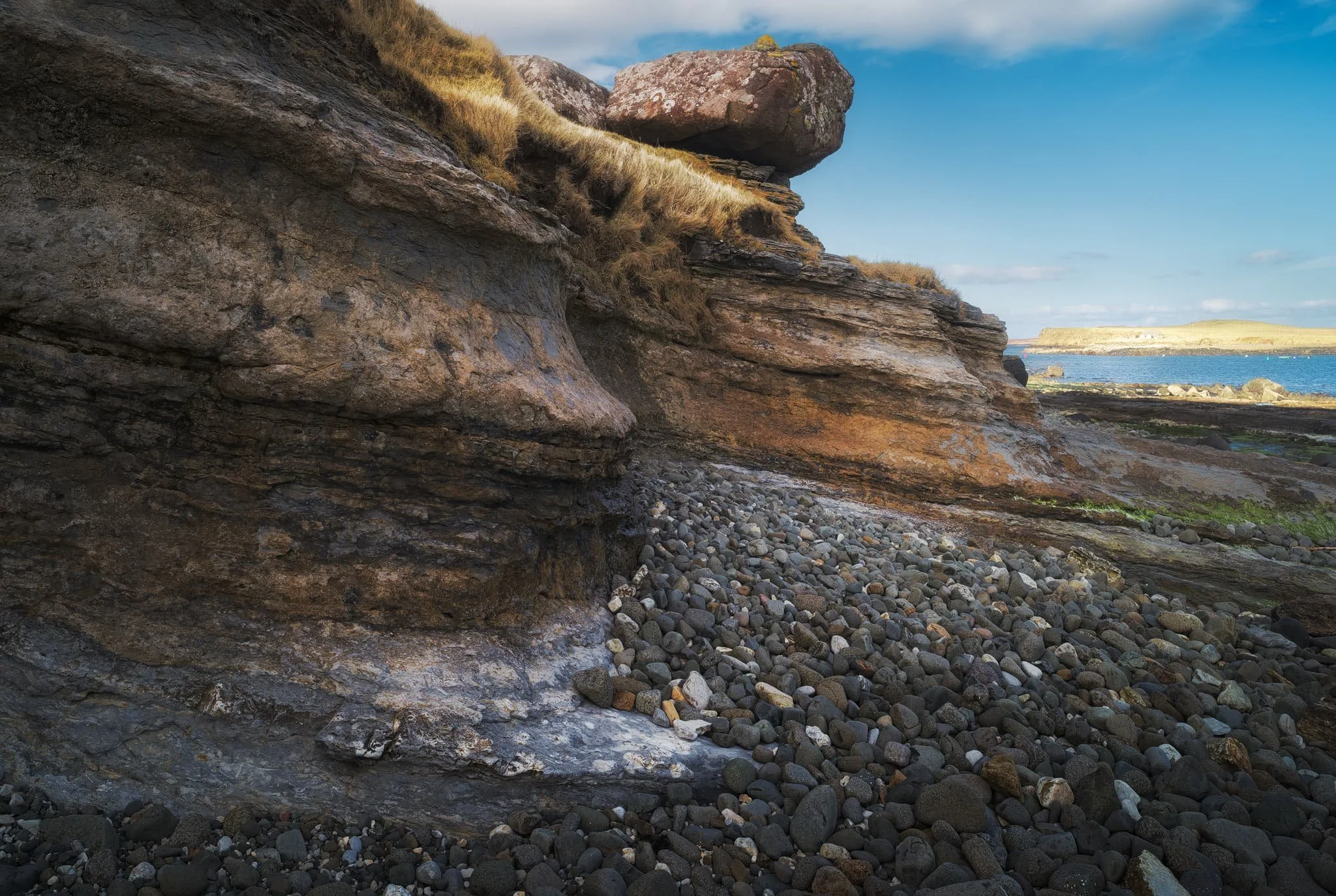 Beautifully sculpted and layered formations give a glimpse of time way before the dawn of humans. In the distance, Staffin island is bathed in golden light.
