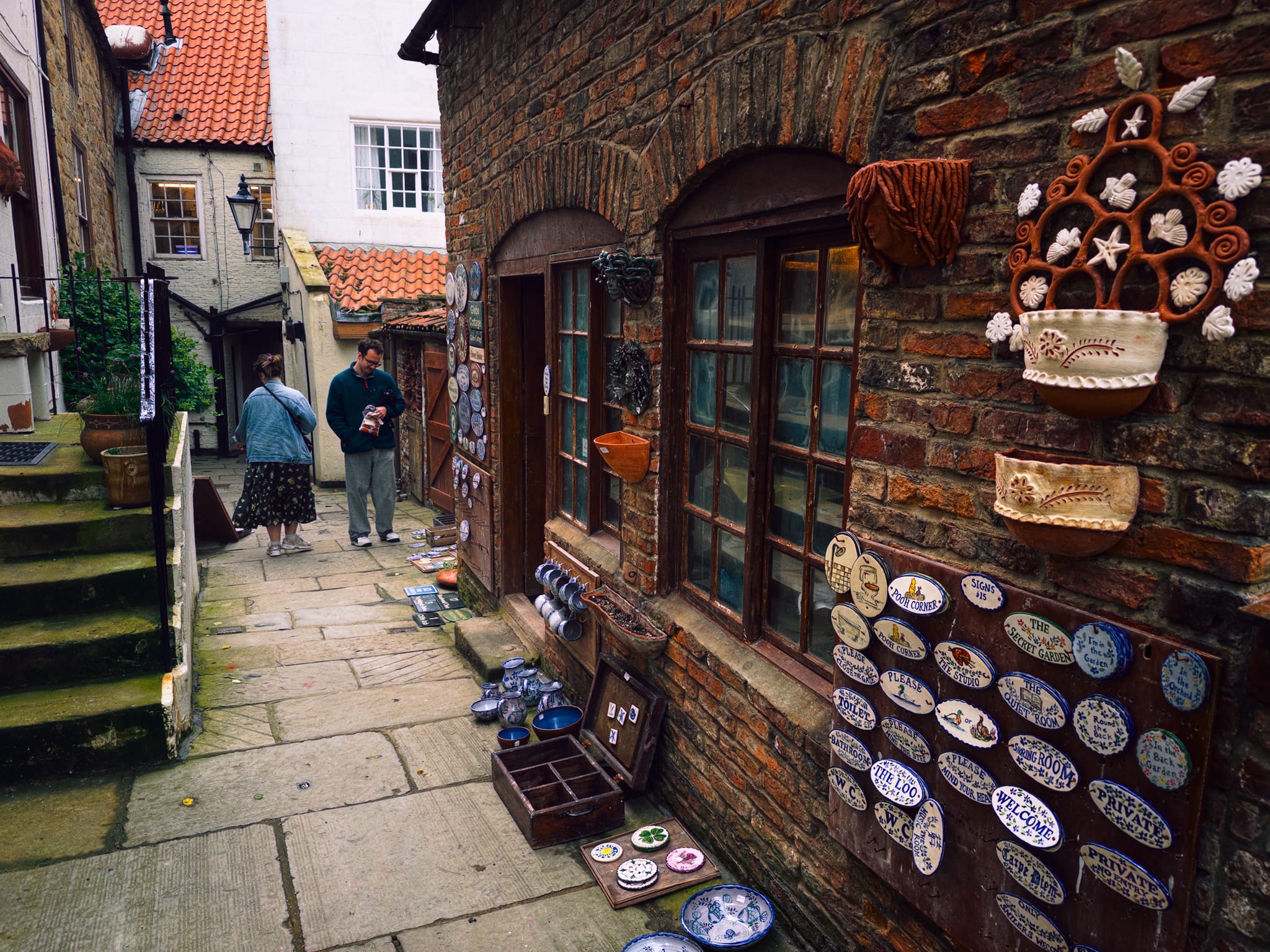Making our way through the old town, Lisabet wanted to take a small diversion to this pottery found down a little ginnel. This is the Washouse Pottery. Laureen Shaw, an Arizonan who settled in Whitby via her grandmother, opened the pottery in 1982 in a former wash house off Church Street. It’s now the town’s oldest surviving pottery.
A ceramics graduate, she pivoted from gallery work to hand-painted tiles after failing to find suitable ones for her own kitchen. Her tiles and commemorative plaques blend Native American and Mexican motifs with British subjects.
